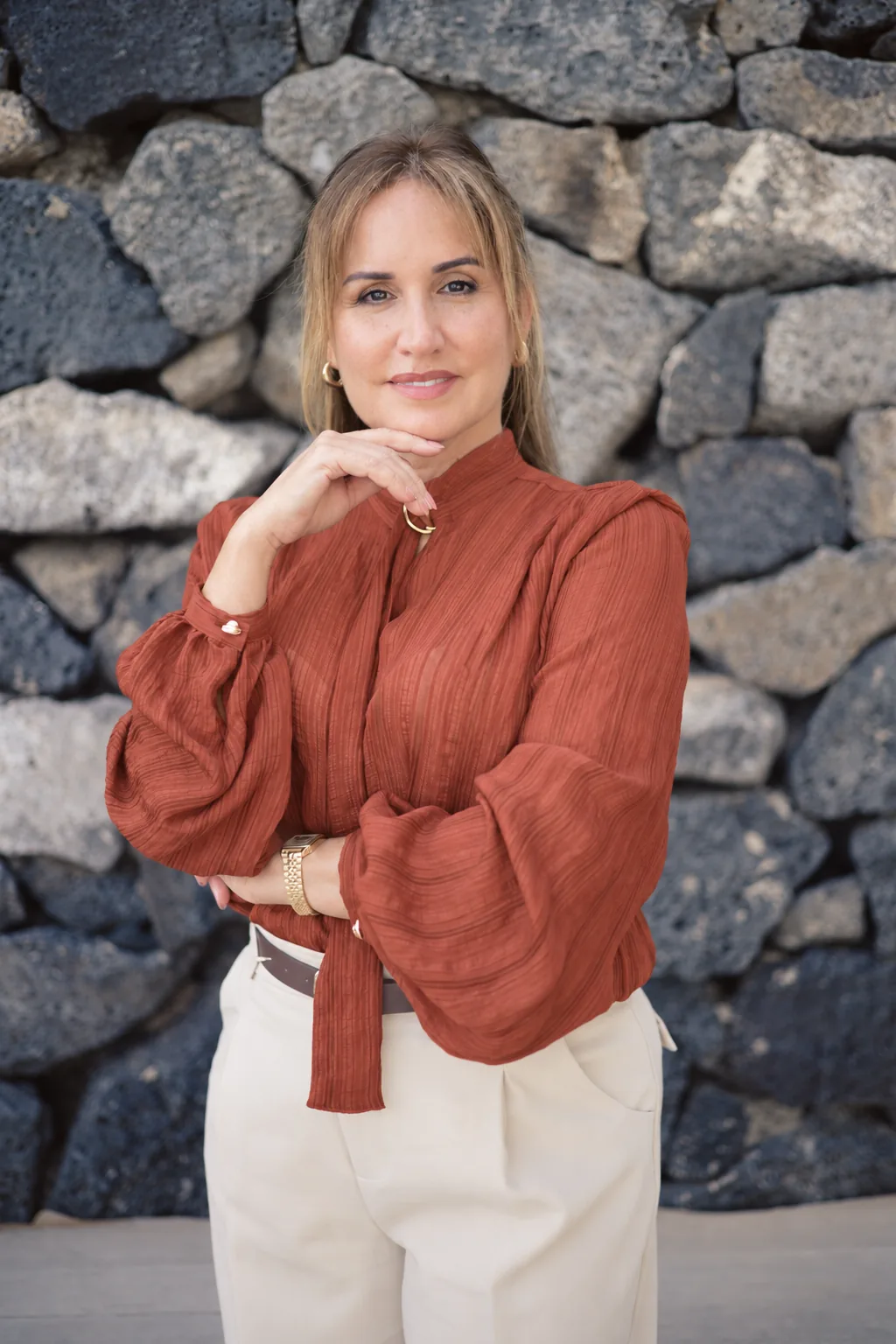 Retrato de Fayna Curbelo con blusa terracota ante un muro de piedra volcánica.