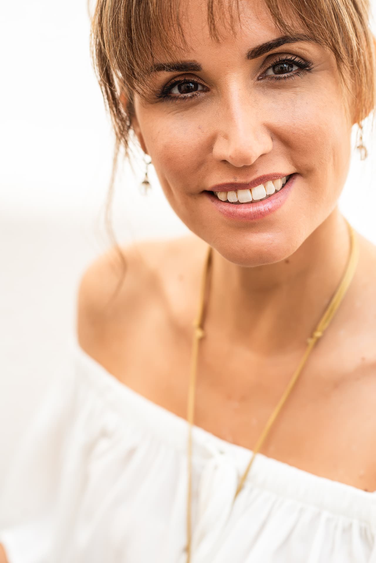 Retrato cercano de Fayna Curbelo sonriendo, con blusa blanca y collar dorado.