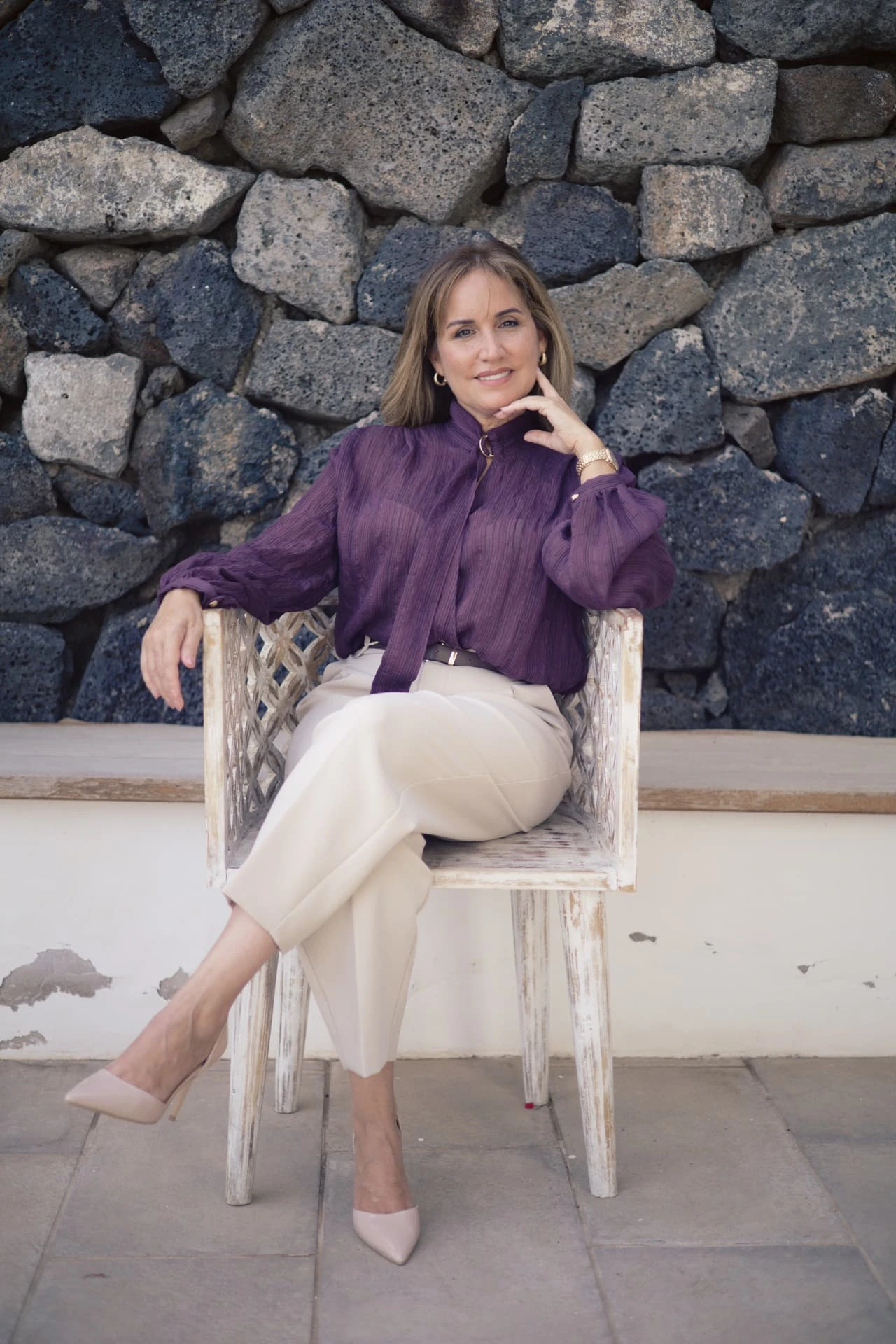 Fayna Curbelo sentada en una silla junto a un muro de piedra volcánica.